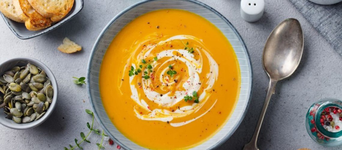 Pumpkin and carrot soup with cream on grey stone background. Top view