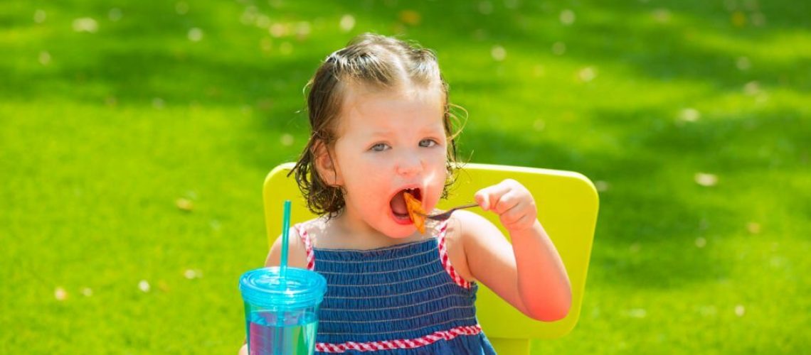 Toddler kid girl eating macaroni tomato pasta in garden turf grass
